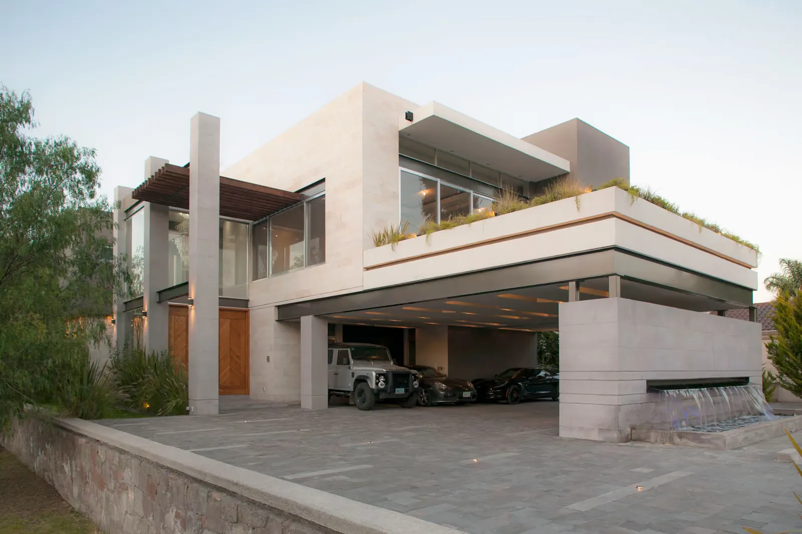 Fachada de dos plantas de Casa AG, con cochera techada bajo la planta alta y una jardinera en el borde de la terraza