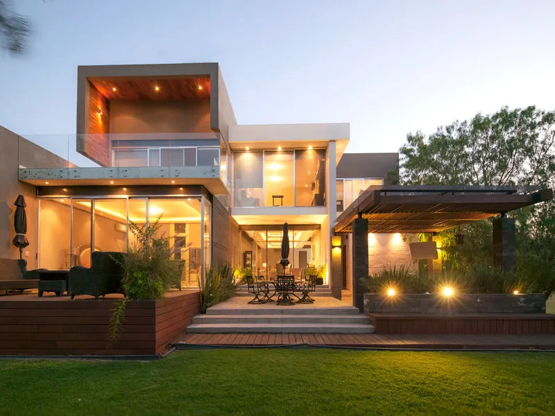 Fachada posterior de Casa AG de noche, con deck de madera y jardín