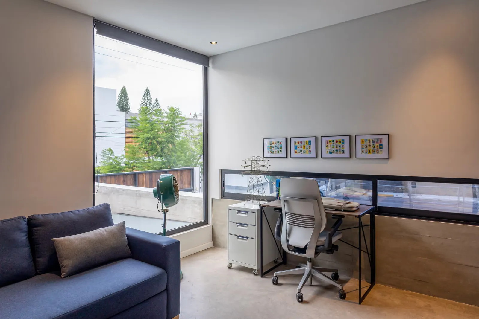 Estudio de la Casa Seto con sofá azul, escritorio y un ventanal que da a los árboles