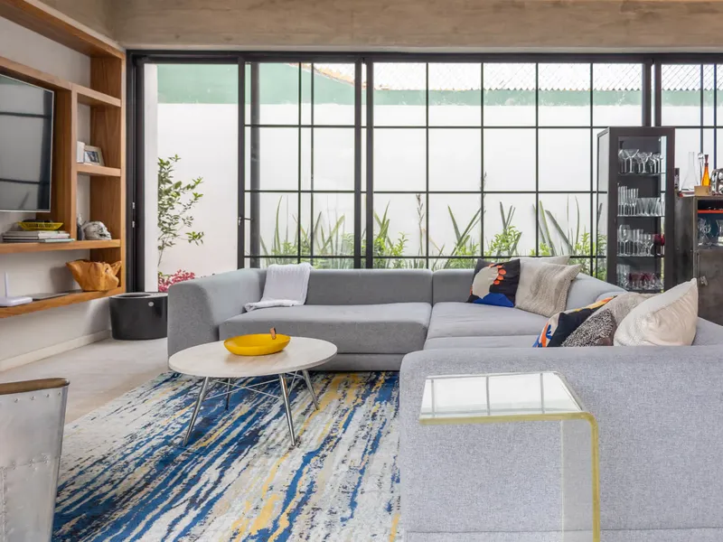 Sala de Casa Seto con sofá gris y ventanal de herrería negra